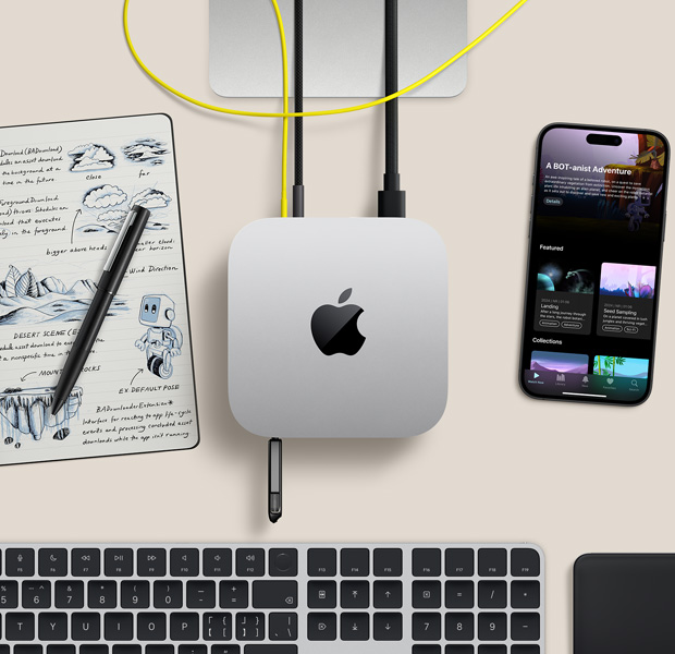 桌上的银色 Mac mini 的俯视图,几根连接线和闪存盘已插入端口,设备旁边摆放着无线键盘、触控板、iPhone 和记事本。