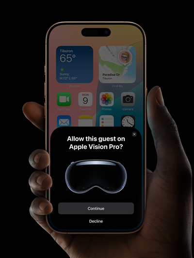 A hand holding an iPhone. The iPhone's screen displays a window with the message, "Allow this guest on Apple Vision Pro?" with buttons labeled "Continue" and "Decline."