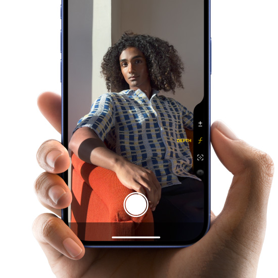 一隻手握著群青色 iPhone 16，拇指在相機控制按鈕上滑動，使用數碼變焦取景構圖