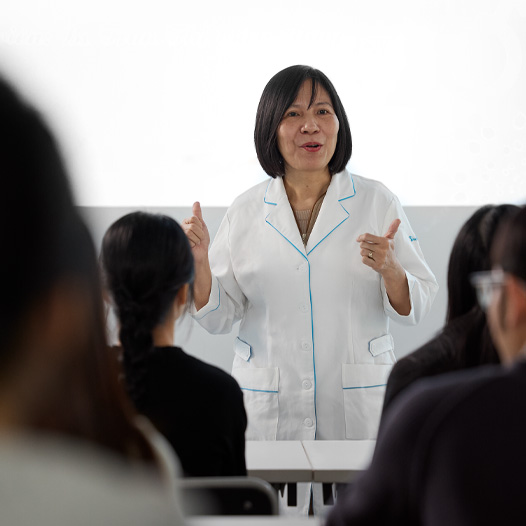 一位穿著白色實驗袍的講師在坐滿學生的教室前面授課