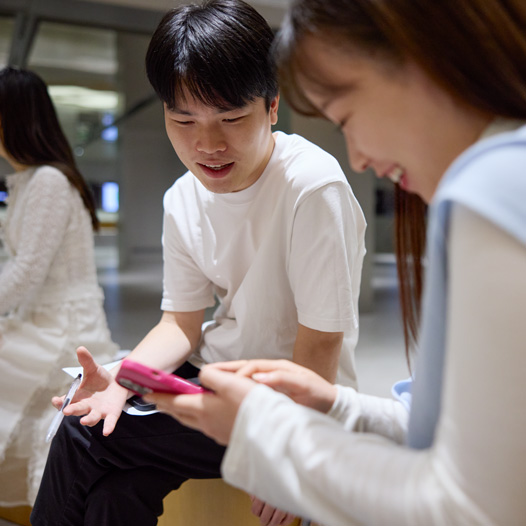 兩個人邊說話邊低頭看著 iPhone，其中一人拿著並操控著 iPhone