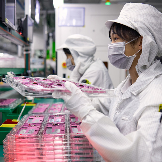 兩位穿著全罩式工作服的員工在組裝工廠處理 iPhone 零件