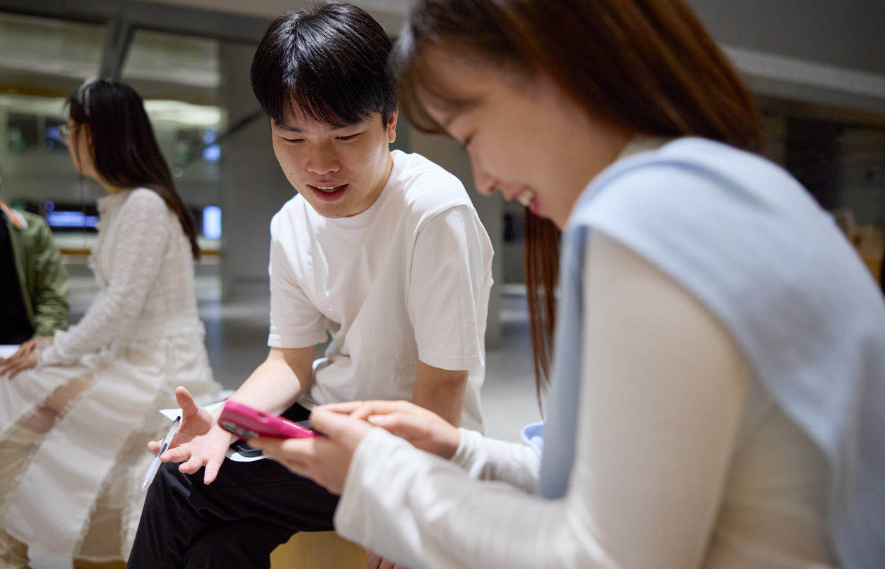 兩個人邊說話邊低頭看著 iPhone，其中一人拿著並操控著 iPhone