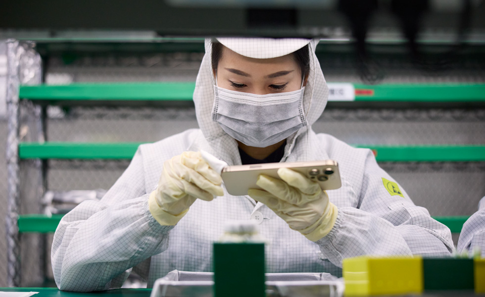一位穿著全罩式工作服的員工在工作崗位用布擦拭 iPhone
