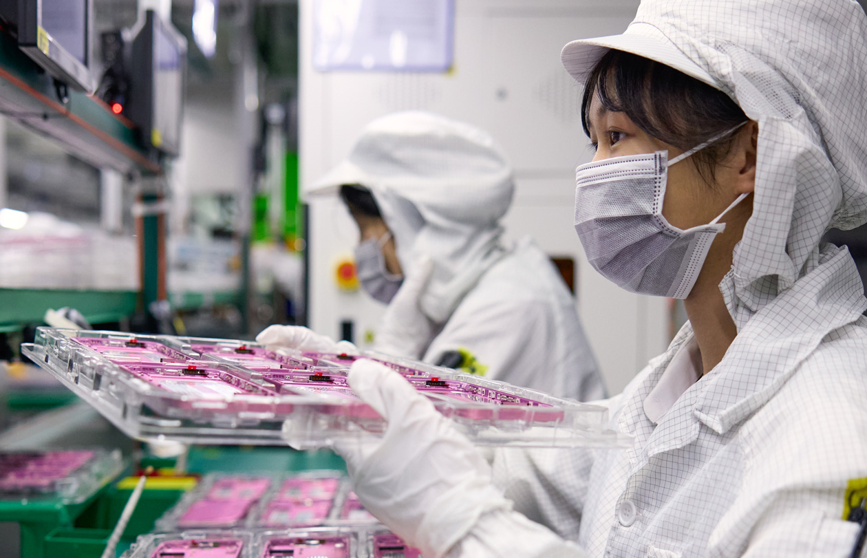 兩位穿著全罩式工作服的員工在組裝工廠處理 iPhone 零件