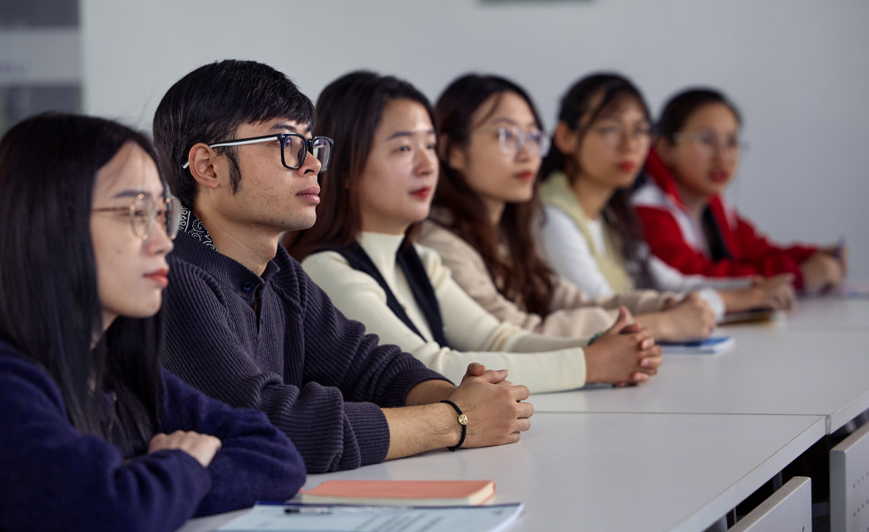 六個人坐在一排長桌前，專注於課室前方的事物