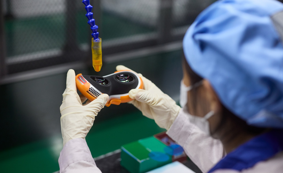在組裝工廠，一位戴有乳膠手套的員工拿著 Apple Vision Pro 的零件