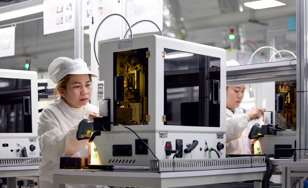 兩位員工身穿工作服，戴著帽子，站在工作崗位操作 Apple Watch 組裝機器